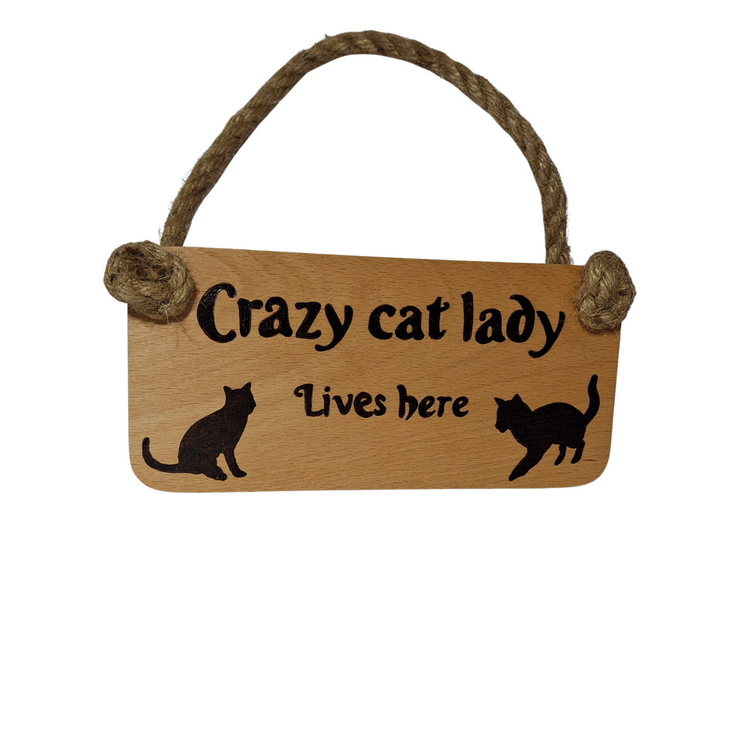 A rectangular wooden sign with a rope handle at the top. The sign has pyrography text and images. The text at the top reads "Crazy cat lady" in a decorative font. Below that, in a smaller, simpler font, it reads "Lives here". On either side of the smaller text, there are two black cat silhouettes facing inwards towards the text.