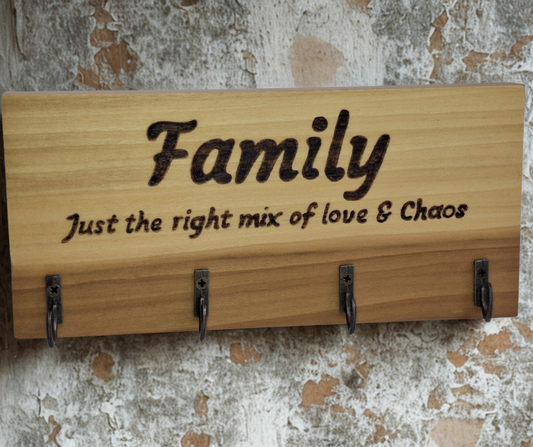 A four-key hook hanger crafted from two-tone Tulipwood, featuring hand-burnt lettering that reads "Family just the mix of love & chaos." The wood has visible grain, showcasing its natural variations.