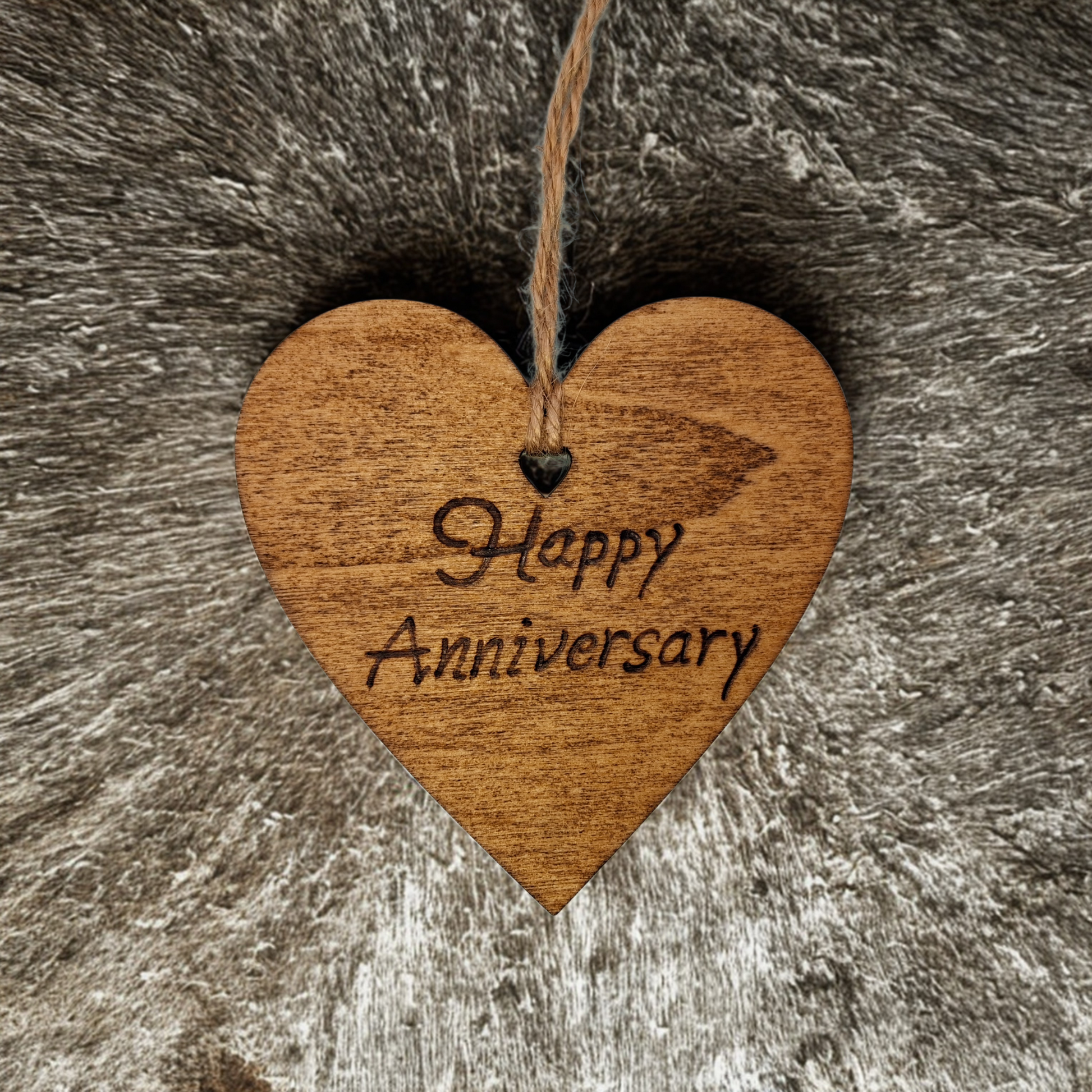 
Heart-shaped wooden ornament, hand-drawn with pyrography, featuring the engraved phrase "Happy Anniversary" in a decorative script, set against a textured background.