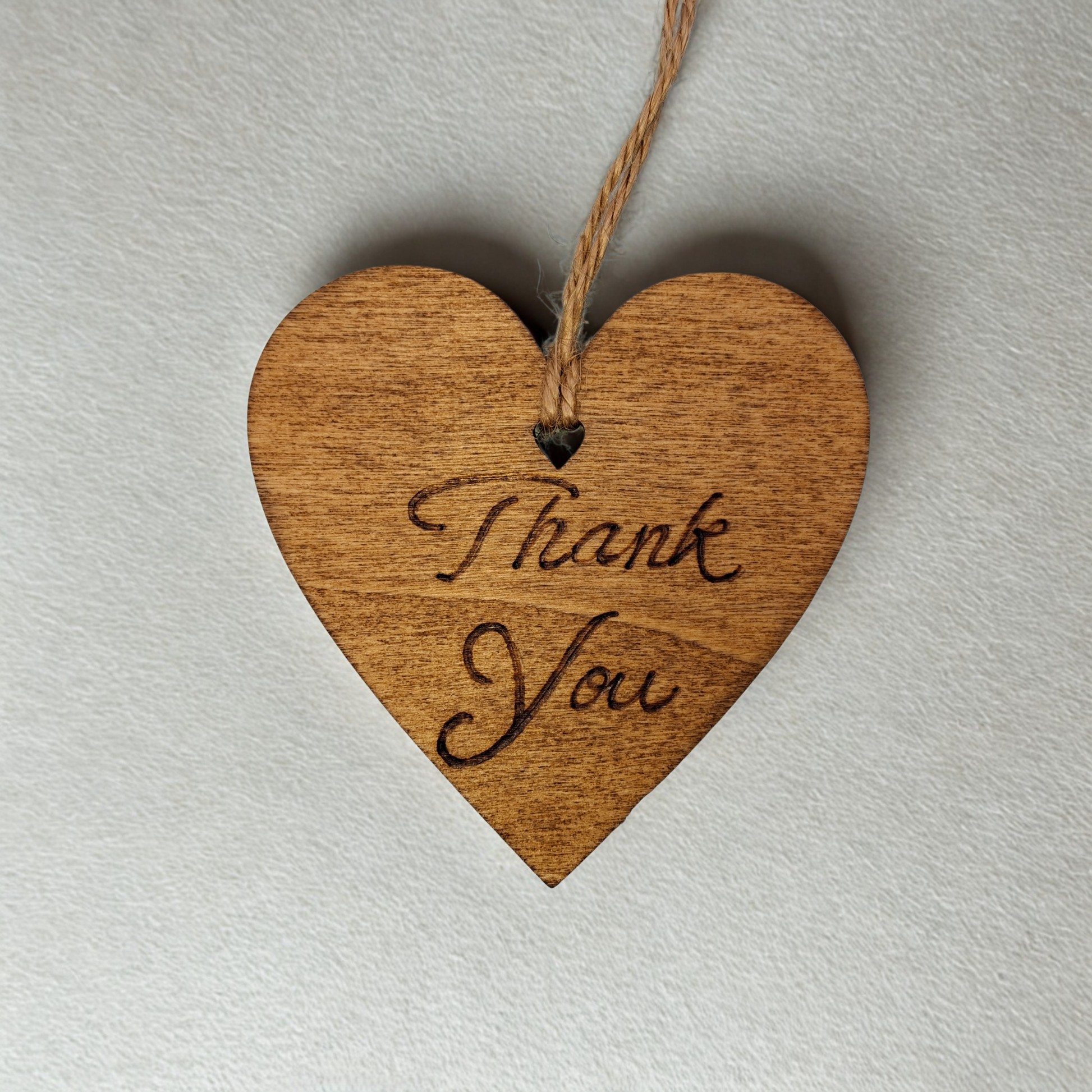 Heart-shaped wooden ornament, hand-drawn with pyrography, featuring the engraved phrase "Thank you" in a decorative script, set against a textured background.