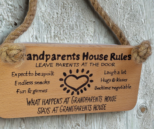 Hand-decorated pyrography sign for grandparents, featuring "Grandparents House Rules" and playful guidelines such as "Leave parents at the door," suspended by a sturdy jute rope.