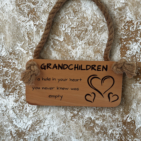 Wooden sign with "Grandchildren, fill a hole in you heart you never knew was empty" hand burnt and hearts hanging on a textured surface