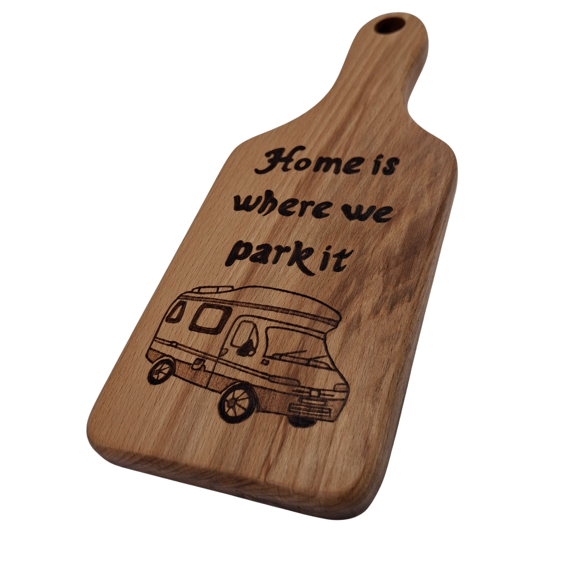 Wooden cutting board with hand burnt text "Home is where we park it" text and camper illustration on a clear background
