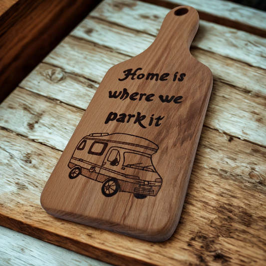 Wooden cutting board with hand burnt text "Home is where we park it" text and camper illustration on a wooden surface