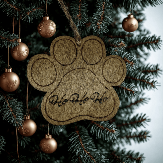 
A wooden Christmas ornament shaped like a dog's paw print. The wood is light brown with visible grain patterns. A twisted twine loop is threaded through a hole at the top for hanging. The words "Ho Ho Ho" are carved into the center of the paw. The background is solid black.