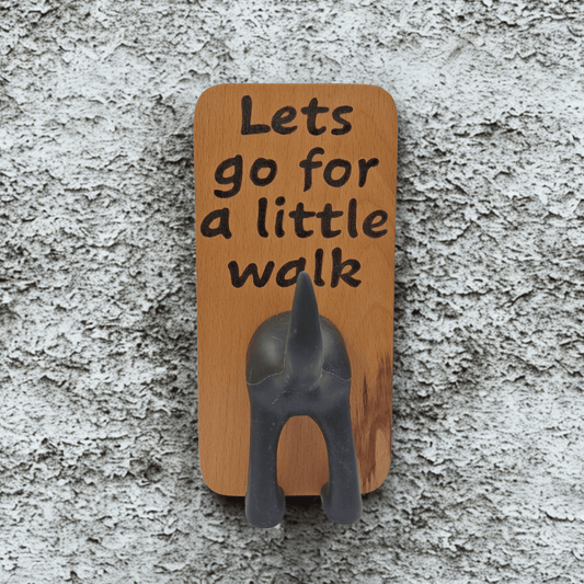 Wooden wall hook featuring the phrase "Lets go for a little walk" created with pyrography (hand burnt lettering). A black dog's rear end forms the hook. 