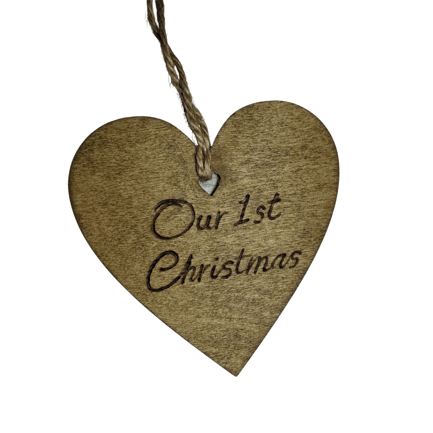 
A close-up of a brown, wooden heart-shaped decoration with a hole at the top. A piece of twine goes through the hole for hanging. The words "Our 1st Christmas" are carved into the front of the heart. The background is solid black.