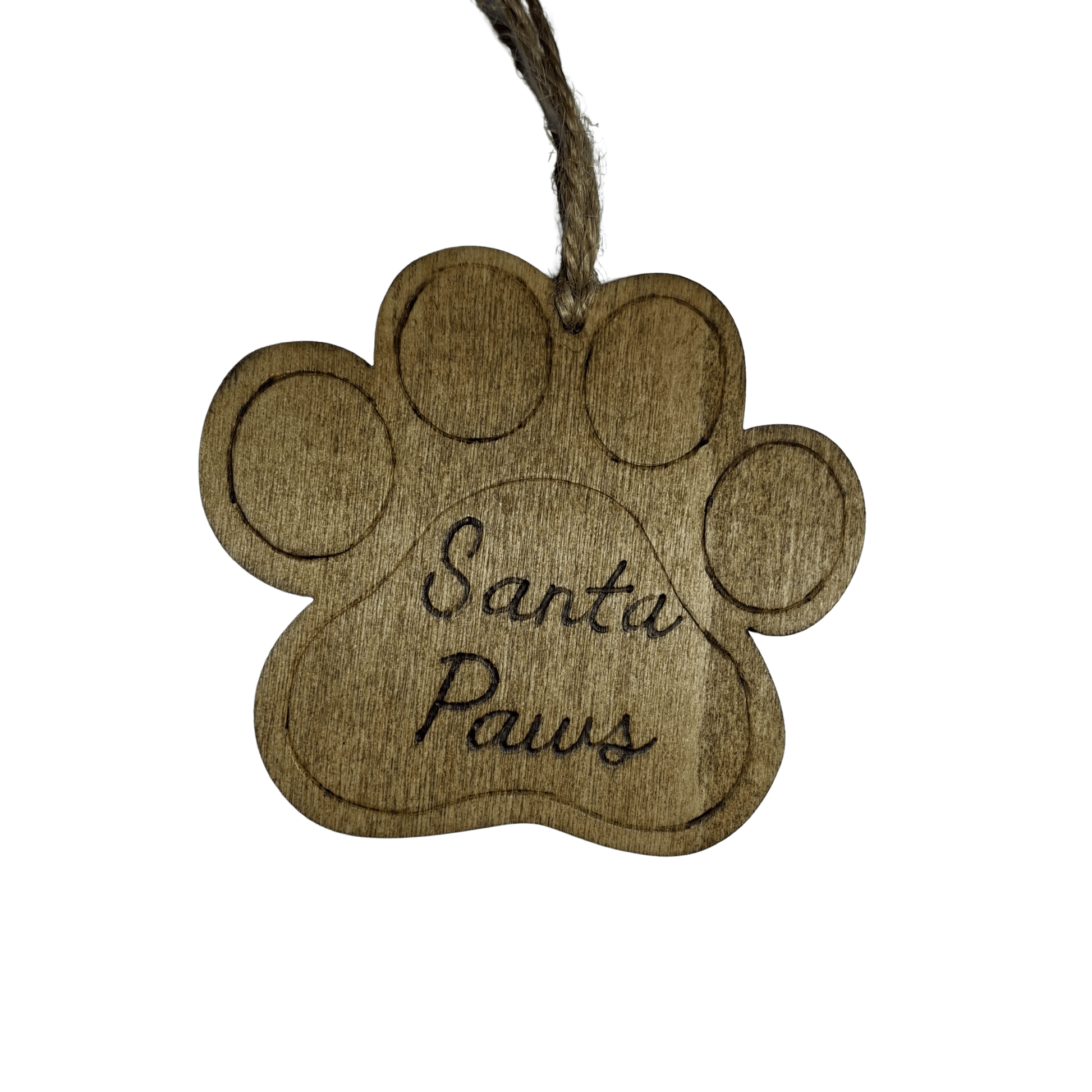 
A light brown wooden decoration in the shape of a dog's paw print. A piece of natural twine is threaded through a hole at the top for hanging. The words "Santa Paws" are carved in a cursive font into the center of the paw. The background is solid black.